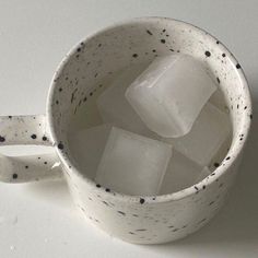 a cup filled with ice cubes sitting on top of a white table next to a wall