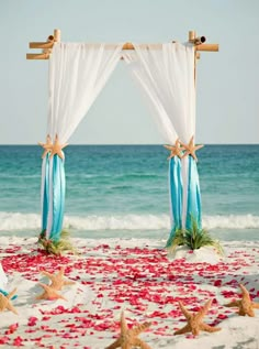 an outdoor wedding setup with starfish on the sand and petals in the ocean water