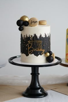 a white and black birthday cake with gold decorations on a table next to a box of cookies