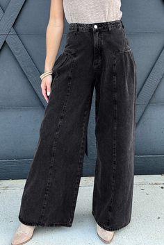 a woman standing in front of a blue wall wearing black wide legged pants and heels