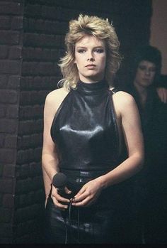 a woman in a black leather dress standing next to a brick wall