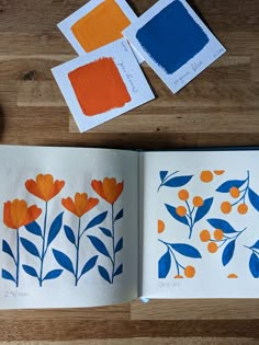 an open book with orange flowers and blue leaves on it next to some paint samples