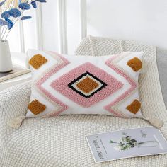 a white and pink pillow sitting on top of a couch next to a vase with flowers