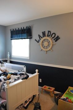 a child's bedroom decorated in blue and white with a ship wheel on the wall