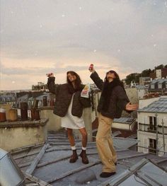 two people standing on top of a roof with their arms in the air and one person holding something up