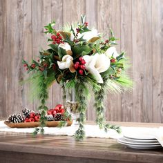 a christmas centerpiece with white flowers, greenery and pine cones on a wooden table