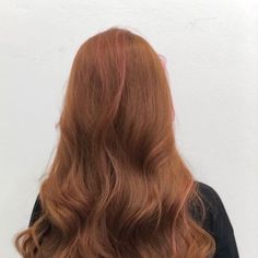 a woman with long red hair standing in front of a white wall wearing a black top