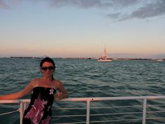 a woman standing on the deck of a boat in the ocean with her arms outstretched