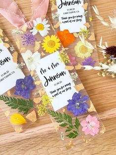 wedding favors with flowers on them sitting on top of a wooden table next to dried flowers