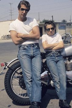 two men sitting on the back of a motorcycle in front of a building with their arms crossed