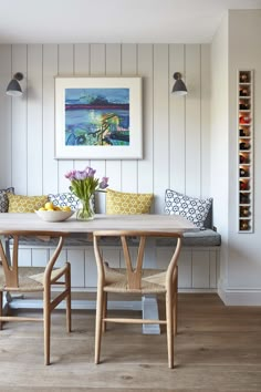 a dining room table and chairs with artwork on the wall above it, along with two vases filled with flowers