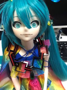 a close up of a doll with blue hair and green eyes wearing a colorful dress