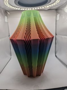 a multicolored vase sitting in the middle of a room with lights around it