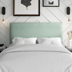 a bed with white sheets and pillows in front of two framed pictures on the wall