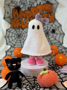 there is a crocheted ghost and two small black cats on the table next to pumpkins