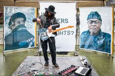 a man standing on top of a stage with a guitar in front of two posters