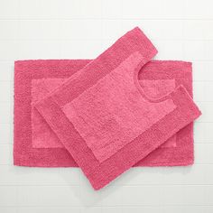 two pink towels on top of each other in front of a white tile wall and floor