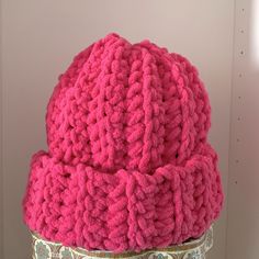 a crocheted pink hat sitting on top of a metal stand next to a wall