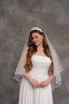 a woman wearing a wedding veil with flowers on the head and shoulder, standing in front of a gray background