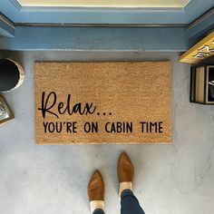 a person standing in front of a door mat that says relax you're on cabin time