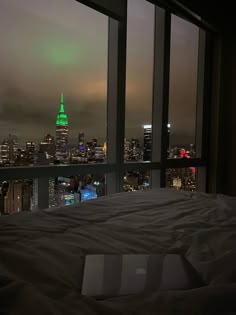 a laptop computer sitting on top of a bed in front of a window overlooking the city