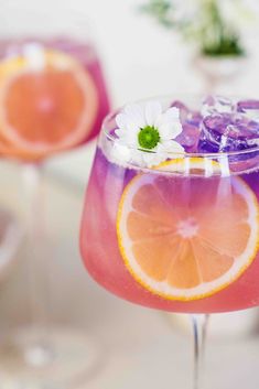 two glasses filled with drinks and garnished with flowers on the rims, sitting on a table