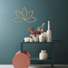 a table with vases and flowers on it in front of a wall painted teal