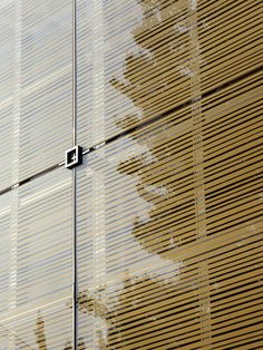 the side of a building with blinds on it's sides and trees reflected in the windows