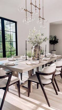 a dining room table with chairs and a vase on the top, in front of a large window