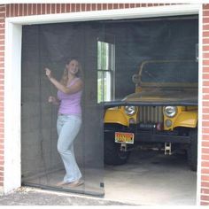 a woman standing in front of a garage door next to a yellow jeep parked inside