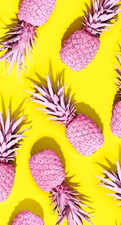 several pink pineapples are arranged on a bright yellow background with shadows from them