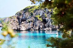 there is a boat that is floating in the water near some rocks and trees on the shore