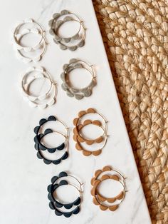 six pairs of hoop earrings sitting on top of a white table next to a straw mat