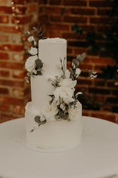 a wedding cake with white flowers and greenery on the top is sitting on a table