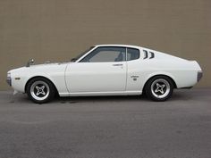 a white muscle car parked in front of a brown brick wall with the door open