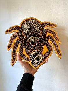 a person holding up a wooden cutout of a spider with skulls on it's face