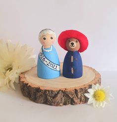 two small figurines sitting on top of a piece of wood next to a flower