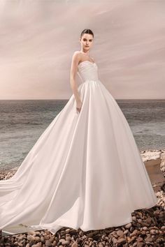 a woman in a wedding dress standing on rocks near the ocean