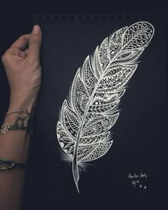 a woman's hand holding up a drawing of a feather