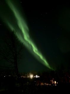 an aurora bore is seen in the night sky above some trees and buildings with lights on them