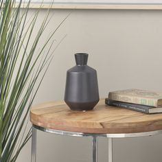 a black vase sitting on top of a wooden table next to a book and plant