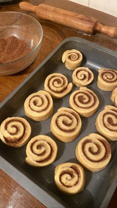 cinnamon rolls on a baking tray with spices and rolling pinwheels in the background