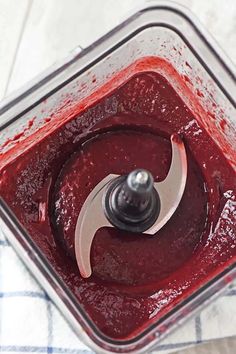 a food processor filled with red liquid on top of a white and blue checkered table cloth