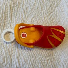 a red and yellow toy shoe laying on top of a white bed next to a pacifier