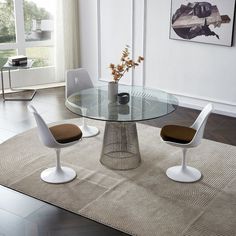 an oval glass table with white chairs and a vase filled with flowers on the side