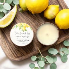 some lemons are sitting on a wooden tray next to a candle and some leaves