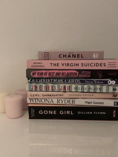 a stack of books sitting on top of a white table next to a small candle