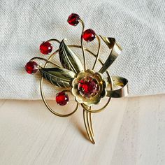 About this item: This is a darling vintage 1940s Harry Iskin Floral Brooch. It's gold with six garnet red crystal gems.  It's marked with the "HI" logo and "1/20 12k GF".  Condition: This is a vinatge item and is in very good condition. It has had one previous owner so some wear is expected. Dimensions: Width: 2" Height: 2 5/8" About the Designer: Harry Iskin is considered an undeservedly forgotten jeweler. However, products marked "HI" are highly collectible. The history of the brand began in 1930, when Harry Iskin founded the eponymous jewelry brand in the United States. Most Harry Iskin jewelry is gold filled, sterling, or vermeil. Yellow gold was used on the entirety of a piece, with rose gold used as a contrasting accent. A common brooch theme is a floral design, with limited use of g Hi Logo, Crystal Flower Bouquet, Red Garnet Crystal, Bouquet Brooch, Garnet Crystal, Brooch Bouquets, Crystal Flower, Red Crystals, Crystal Gems