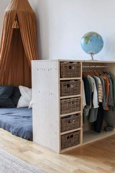 a bedroom with a bed, hanging clothes and baskets on the shelves next to it