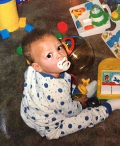 a baby is sitting on the floor with toys around him and drinking from a sippy cup